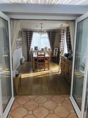 A dining area with a wooden table and chairs, a window with curtains, and a view of the outside. - Plas Tirion (Abergele)