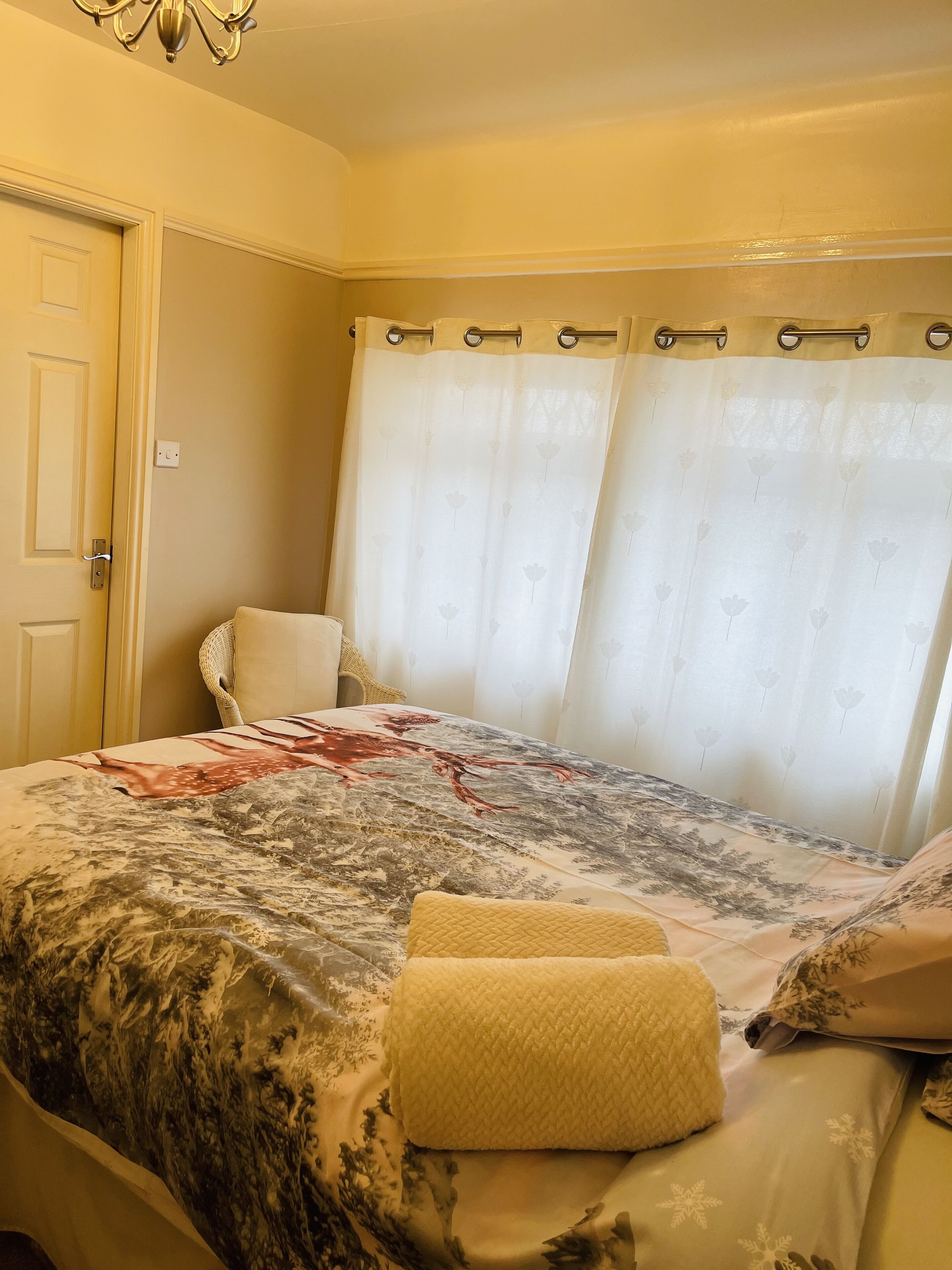 Un dormitorio con cama, una silla y una ventana con cortinas.