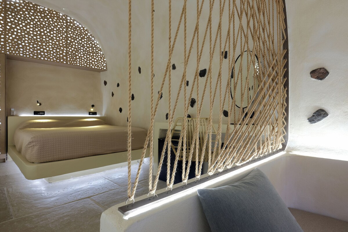 A room with a bed, a hanging rope swing, a window, and a wall with decorative elements.