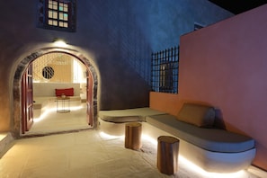 Ein gemütliches Interieur mit einer gebogenen Couch, einem kleinen Holzschemel und einer Sitzecke mit einem roten Kissen.