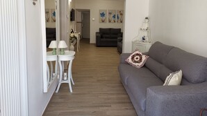 A modern living room with a grey sofa, a small white table with two lamps, and a decorative vase with flowers. - Magnolia House (Montalbano)