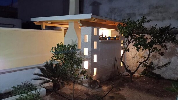 A small, enclosed outdoor area with a wooden structure, possibly a gazebo, surrounded by plants and a white wall. - Magnolia House (Montalbano)
