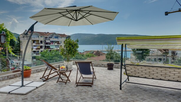 Eine Terrasse mit Meerblick, ein Tisch mit einer Flasche und Obst sowie ein Stuhl.
