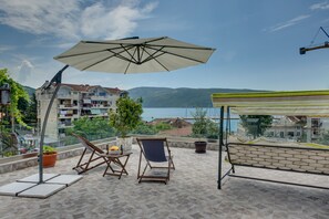 En terrasse med havudsigt, et bord med en flaske og frugt, samt en stol.