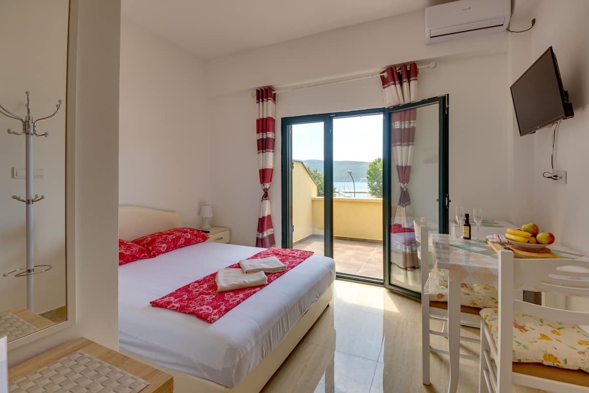 A hotel room with a bed, a table with a fruit bowl, a TV, and a balcony with a view.