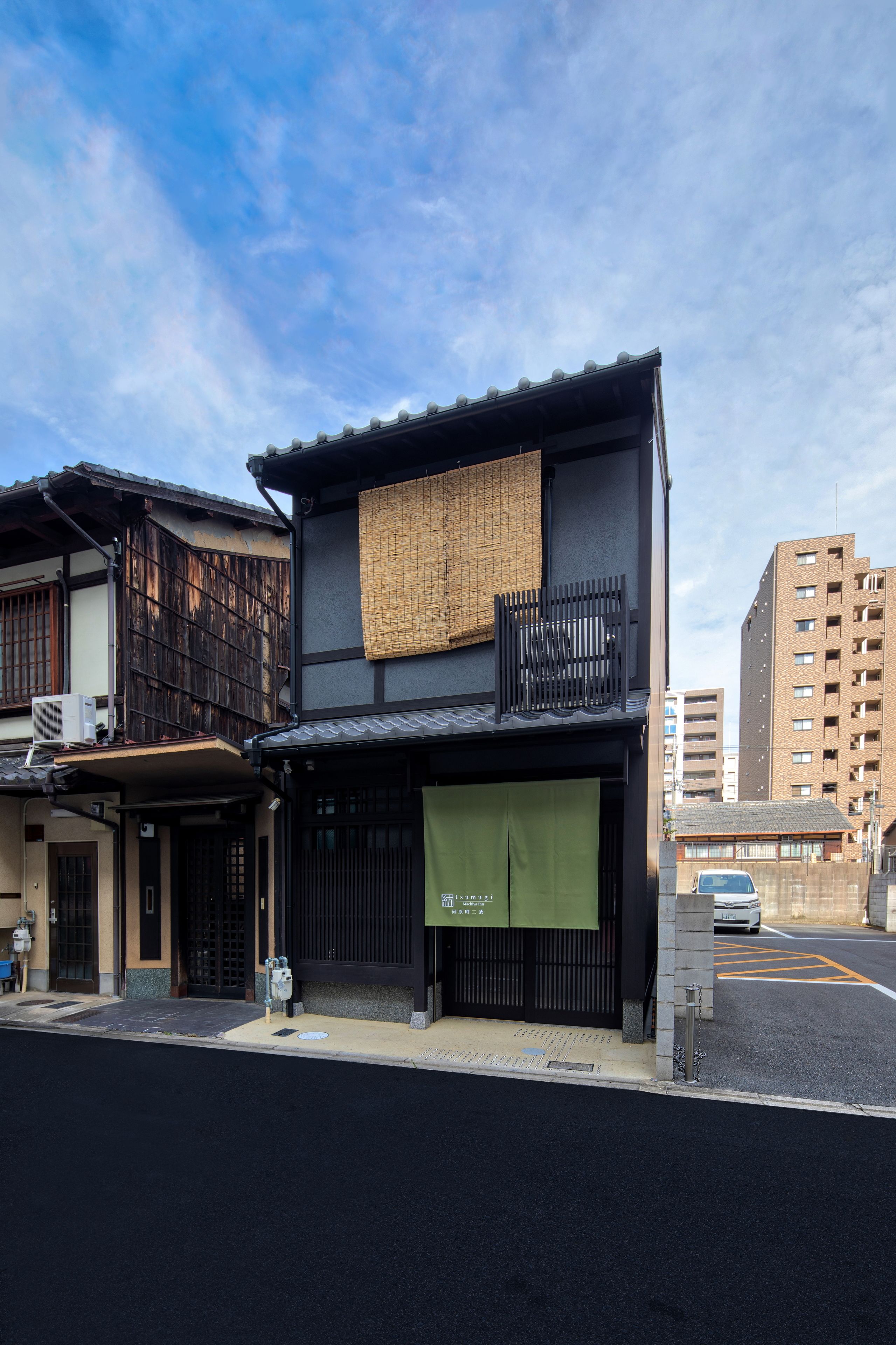 A modern building with a black facade, a green awning, and a traditional wooden structure adjacent to it.