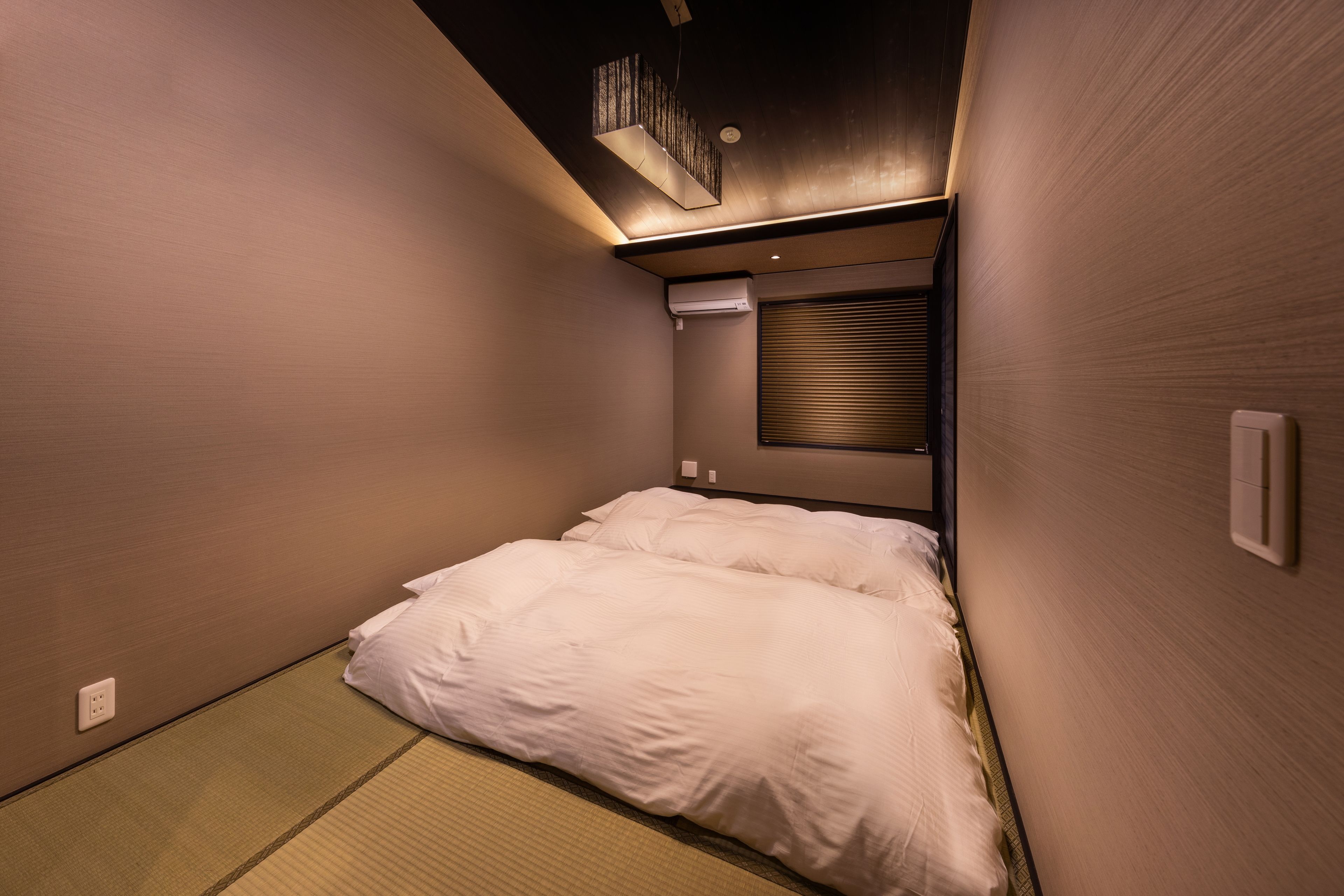 A hotel room with a bed, a ceiling light fixture, and a window with blinds.