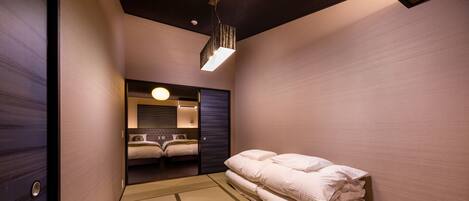 A hotel room with a traditional tatami mat floor, a bed with neatly folded white linens, and a modern ceiling light fixture.