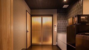 A hallway with wooden flooring, a sliding door with vertical blinds, a refrigerator, and a microwave on a counter. - Kanade Kawaramachinijo (Kyoto)