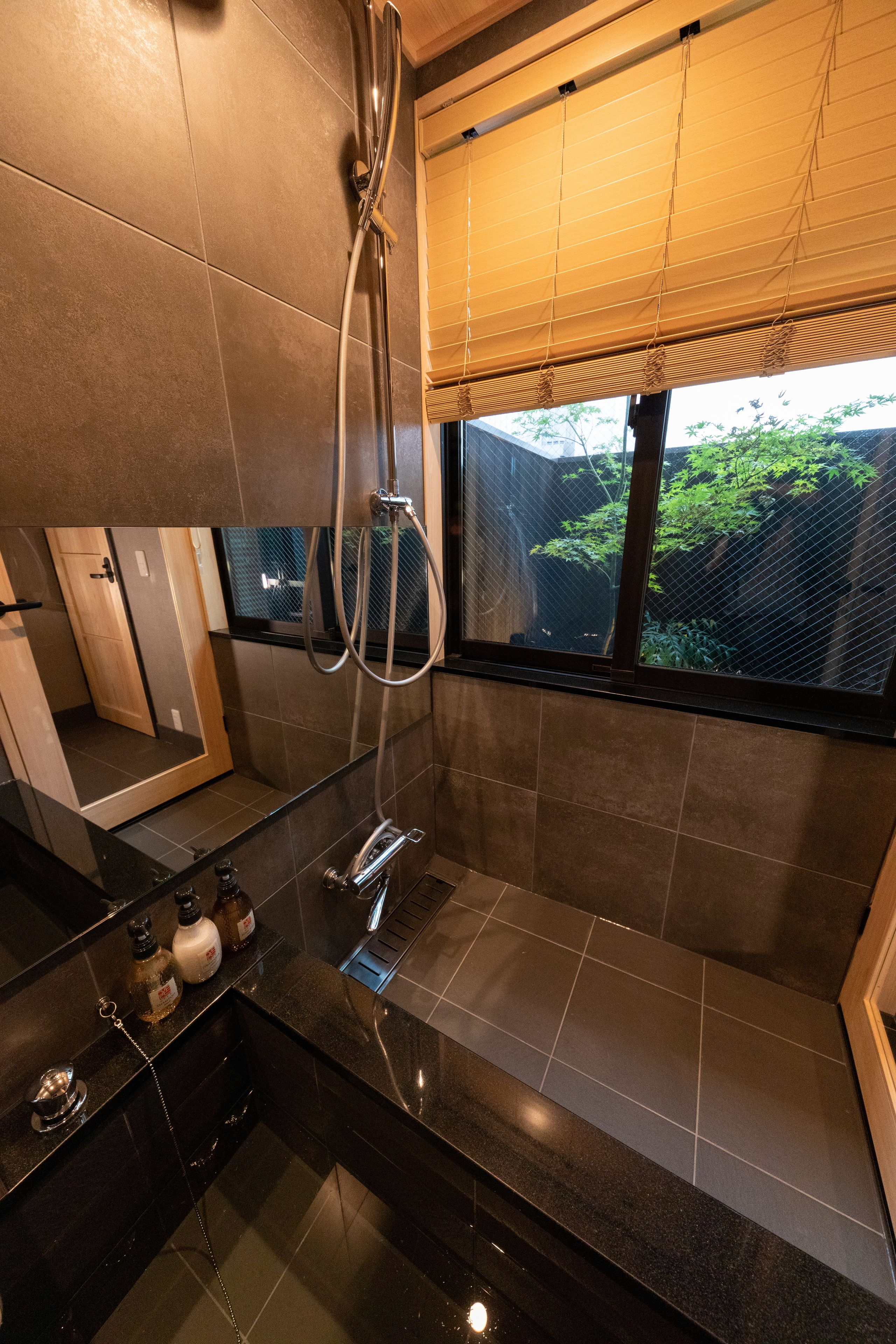 A modern bathroom with a shower, a sink, and a window with a view of greenery.