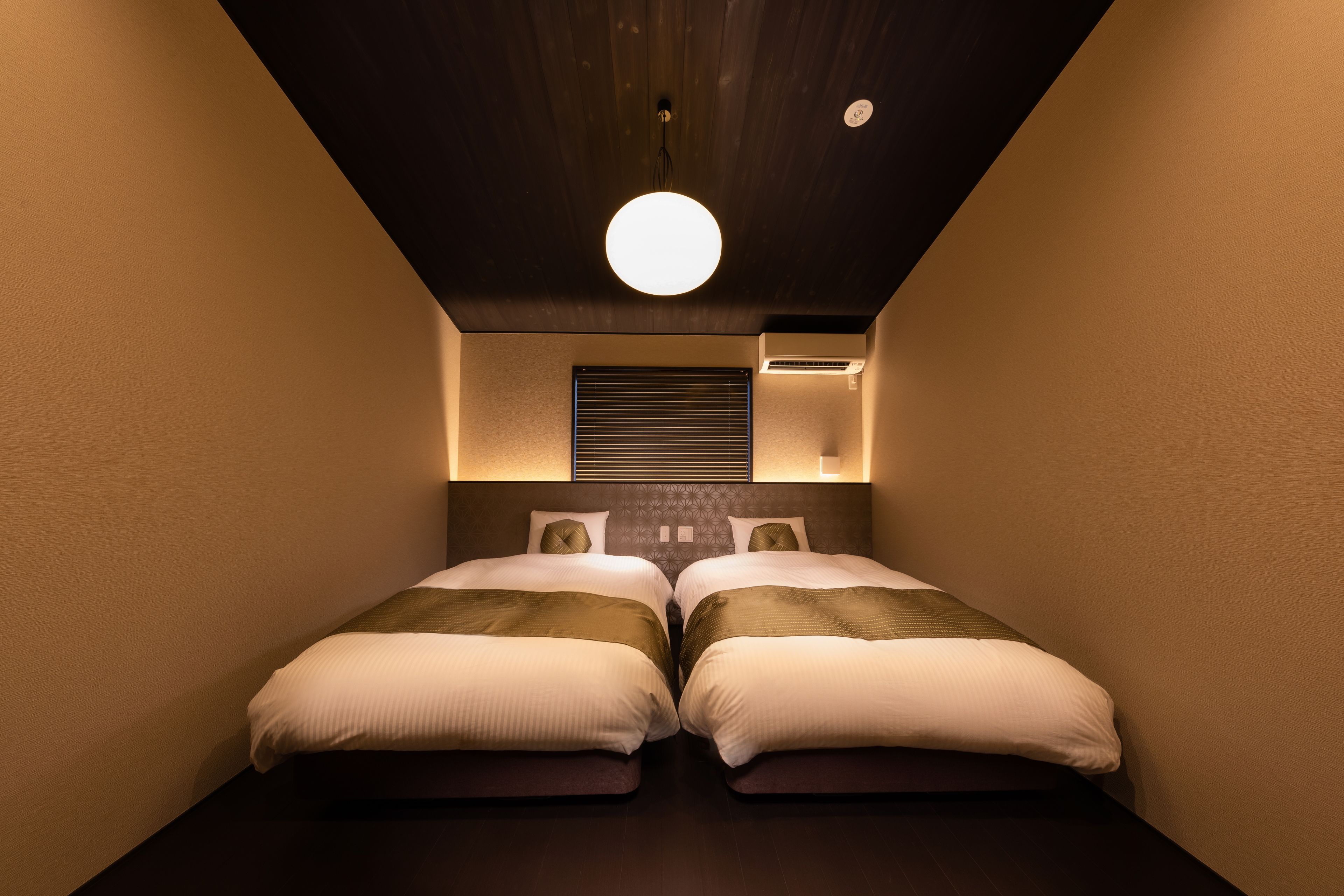 Un dormitorio con dos camas, una lámpara redonda en el techo y un aire acondicionado de pared.