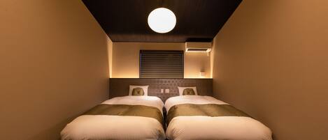 Un dormitorio con dos camas, una lámpara redonda en el techo y un aire acondicionado de pared.