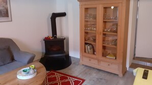 A living room with a sofa, a wooden cabinet with glass doors, a black stove, and a red patterned rug. - off in the summer 08 (Jabel)