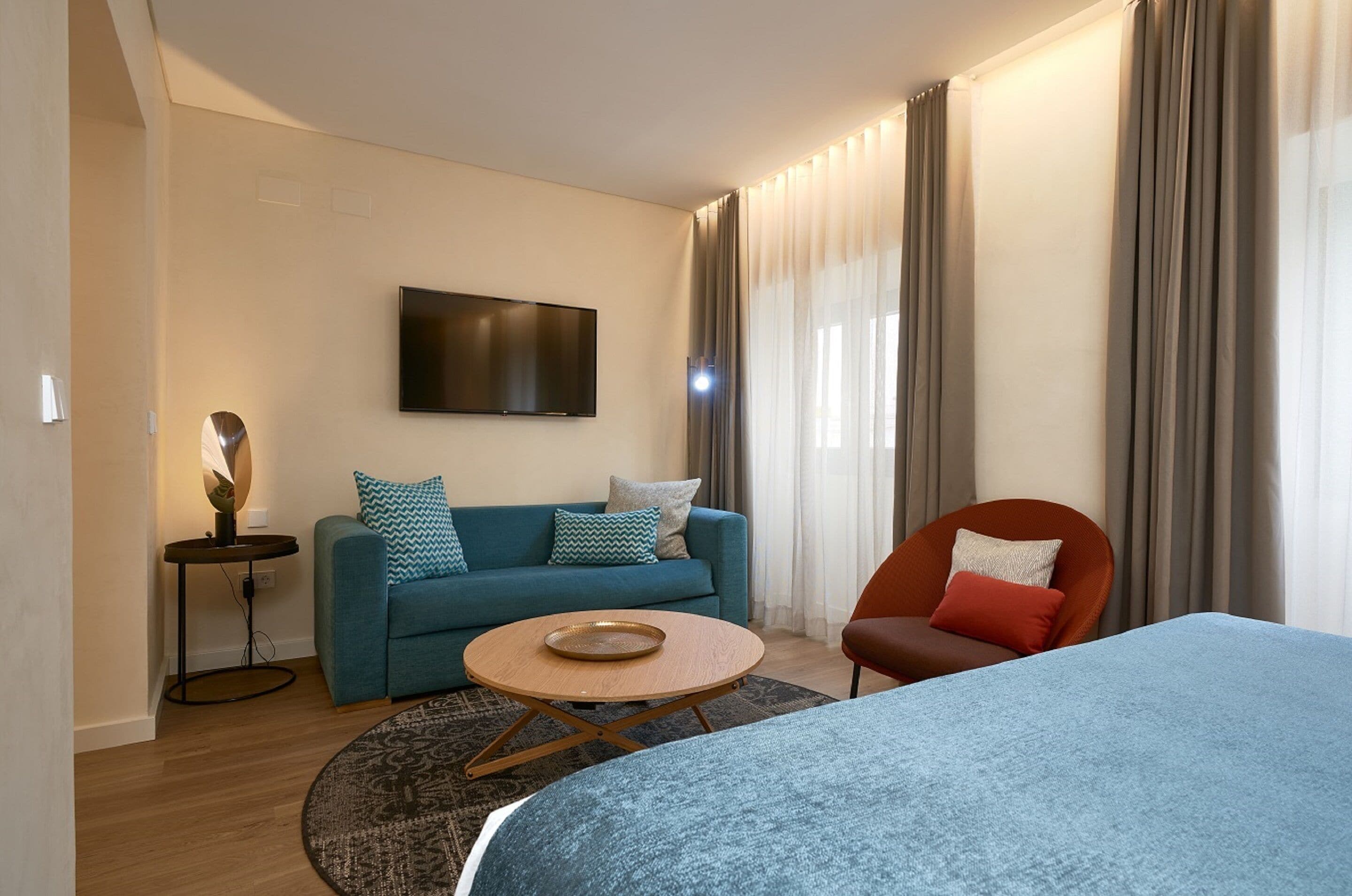 Una camera d'hotel moderna con un divano, un tavolino rotondo, una televisione a schermo piatto e un letto.
