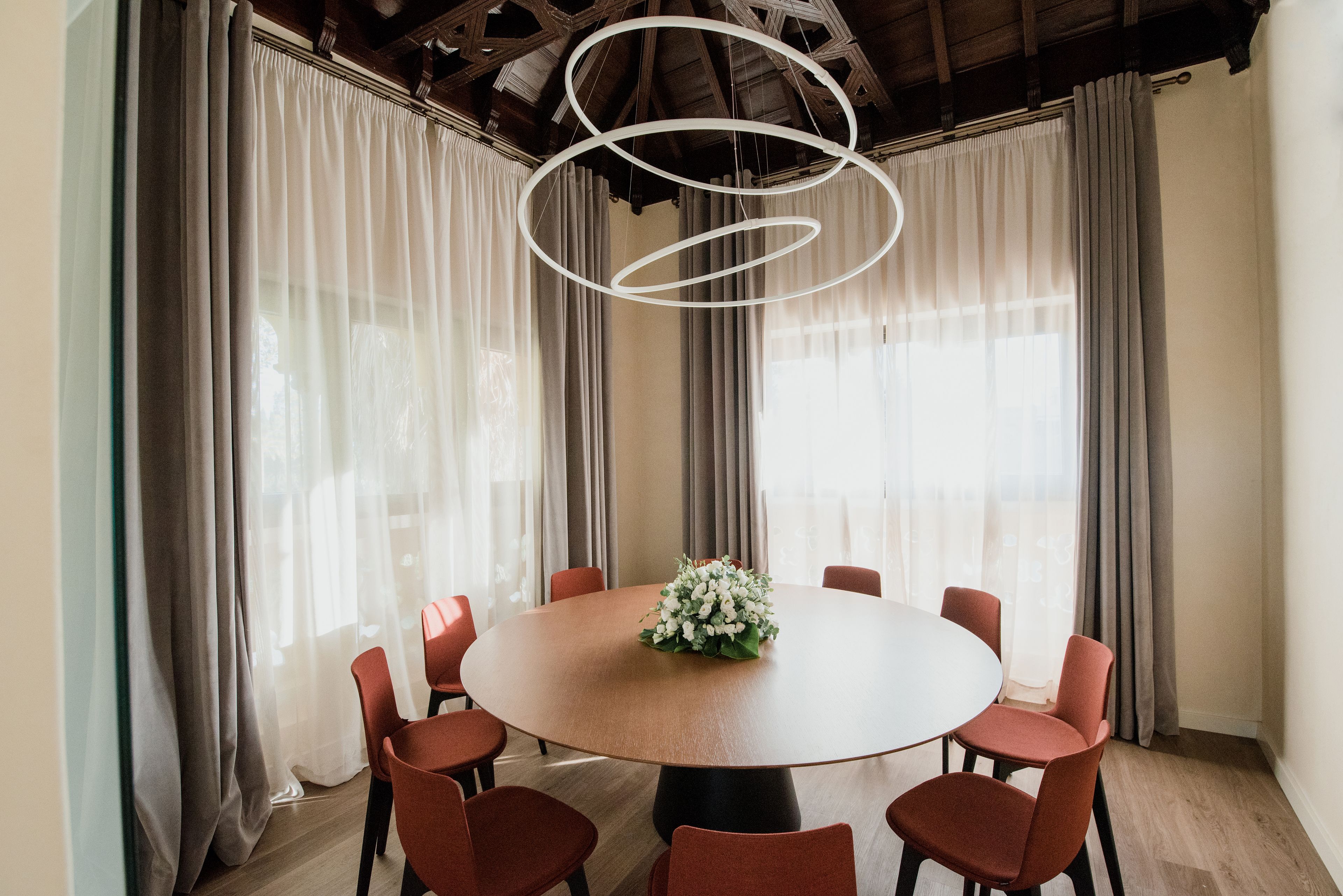 Una mesa redonda para comer con seis sillas, un centro de mesa floral y una lámpara moderna.