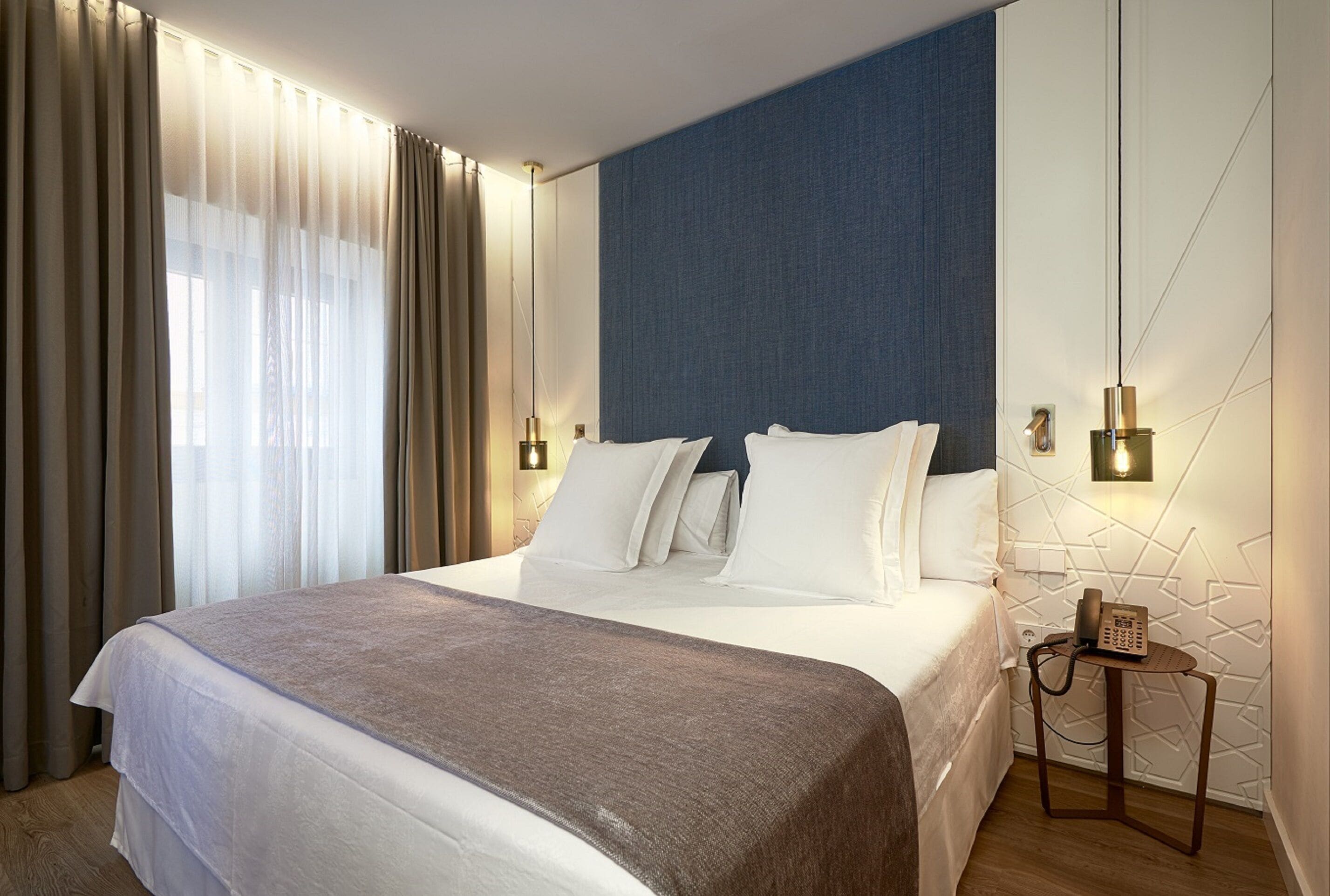 A modern hotel room with a large bed, a blue accent wall, and a bedside telephone.