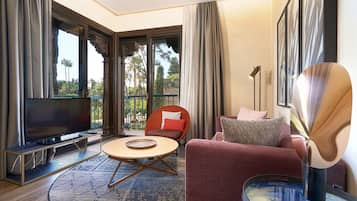 A modern living room with a flat-screen TV, a round coffee table, a red sofa, and a balcony with a view of palm trees.