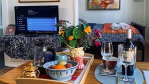 Un salon chaleureux avec une table basse en bois, un ordinateur portable, une plante en pot, un saladier de fruits, une bouteille de vin et des verres.