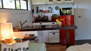Une cuisine avec des meubles blancs, un réfrigérateur rouge et un évier. On y trouve des livres et un vase avec des fleurs sur le comptoir.