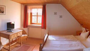 Un dormitorio con techo de madera, una cama, un escritorio con silla y un ventanal con cortinas.