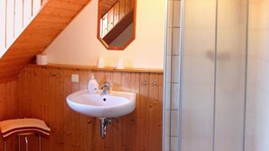 Un baño con detalles de madera, un lavamanos blanco, un inodoro y una zona de ducha.