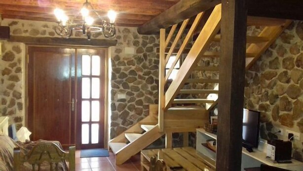 A rustic interior with a stone wall, wooden staircase, and a wooden door.
