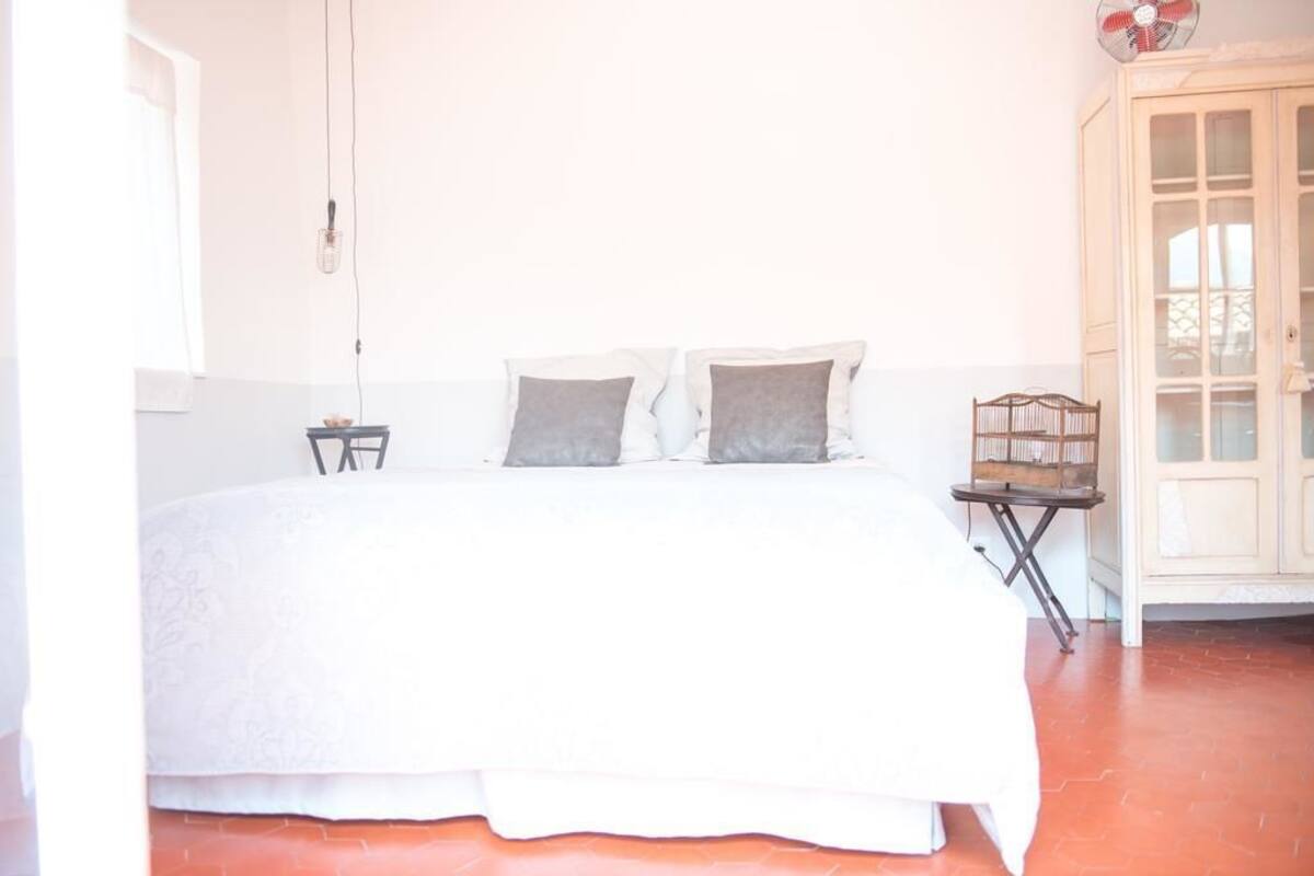 A bedroom with a bed, pillows, a nightstand, a small table, and a cabinet.