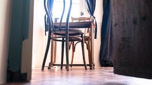Una habitació amb terra de fusta, una cadira de fusta i una finestra amb cortines.