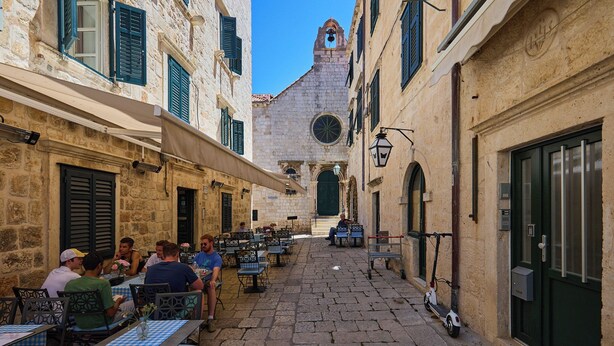 A narrow street with outdoor seating, stone buildings, and a bell tower. - Hedera Estate, Hedera A21 Apartment (Dubrovnik)