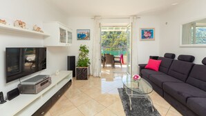 A modern living room with a flat-screen TV, a dark sofa, a glass coffee table, and a potted plant. - Hedera Estate, Hedera A24 (Dubrovnik)