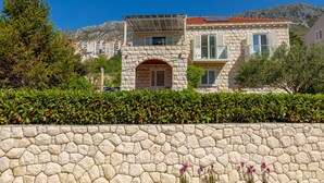 A stone building with a red-tiled roof, a stone wall in front, and a mountain in the background. - Hedera Estate, Hedera A24 (Dubrovnik)