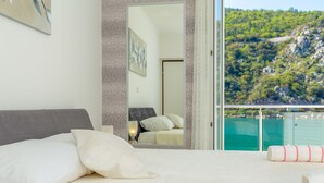 A bedroom with a bed, pillows, a mirror, and a balcony with a view of a green hillside. - Hedera Estate, Hedera A24 (Dubrovnik)