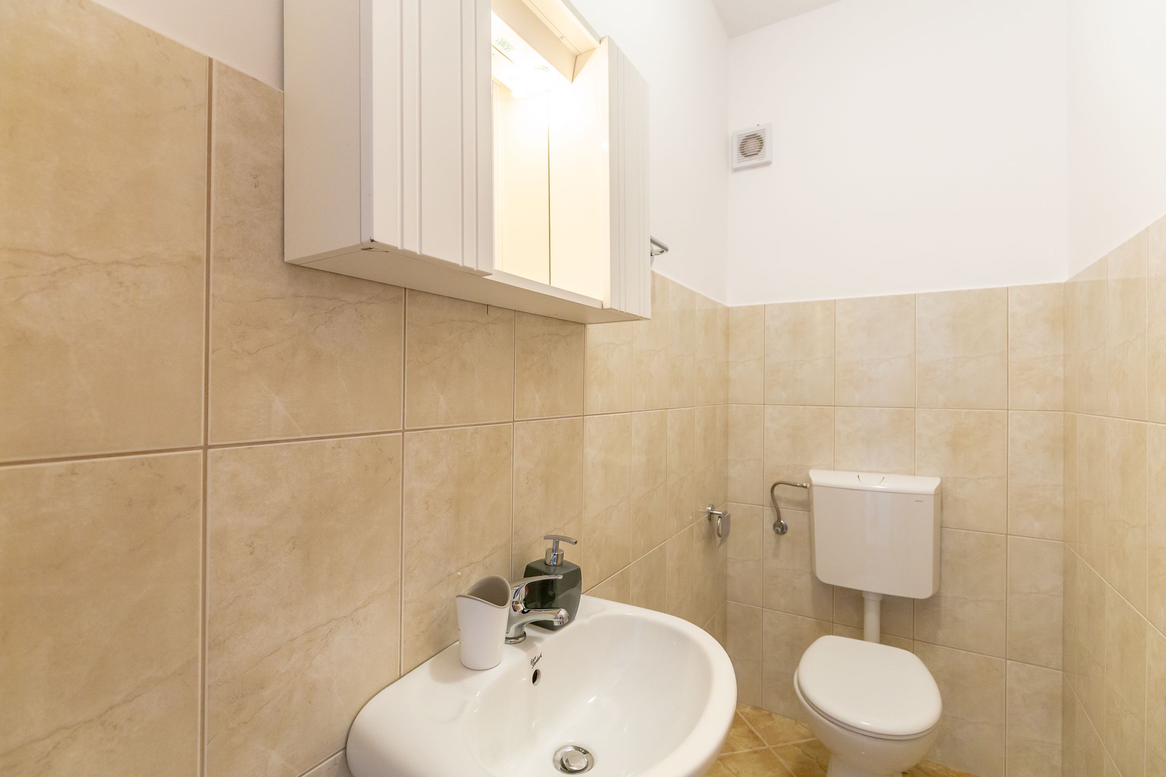 Een badkamer met beige tegels, een wit wastafelmeubel, een spiegel en een toilet.