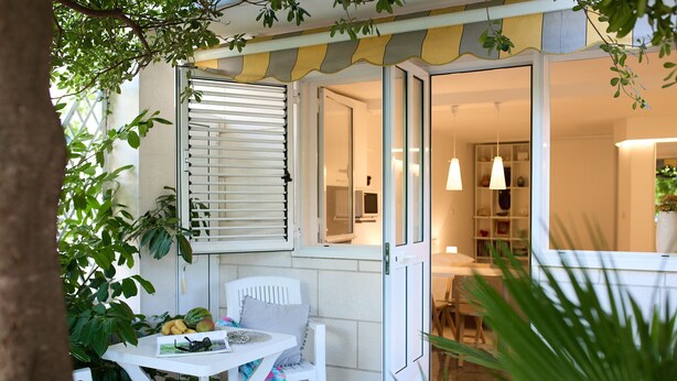 A patio with a white table and chairs, a window with blinds, and a view into the interior of a house. - Hedera Estate, Hedera Studio 6 (Dubrovnik)