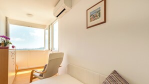 A bedroom with a bed, a chair, a desk, a window with a view, and an air conditioner. - Hedera Estate, Hedera A13 (Dubrovnik)
