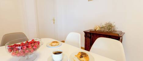 A dining table with a bowl of cherries, a cup of coffee, and a plate with a pastry.