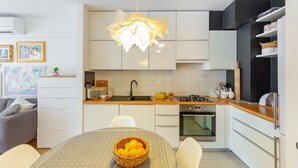 A modern kitchen with white cabinets, a central island with a basket of lemons, a hanging pendant light, and a dining area with a table and chairs. - Hedera Estate, Hedera A29 (Dubrovnik)