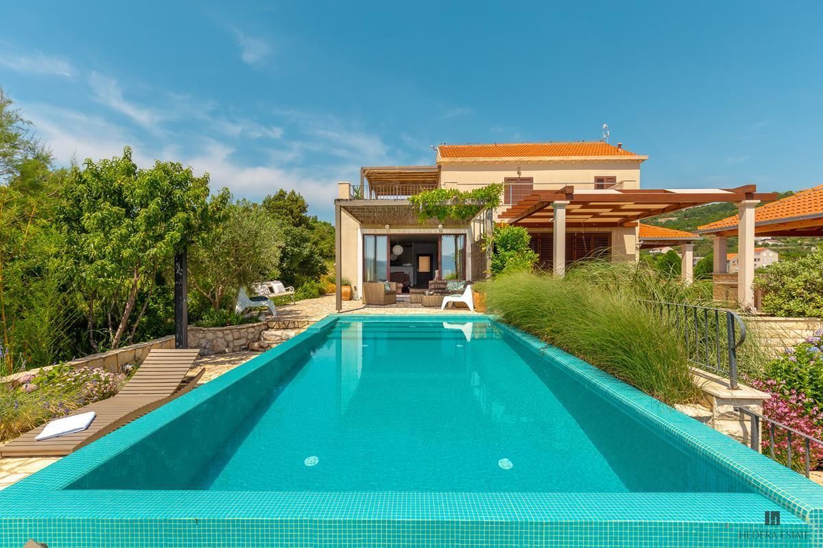A modern poolside area with a clear blue pool, a house in the background, and lush greenery.