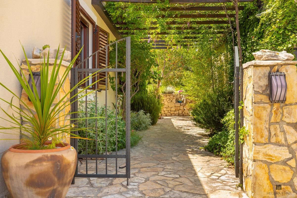 A stone pathway leading to a house with a pergola covered in greenery.