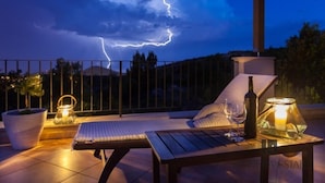 A balcony with a table, chairs, and a bottle of wine, set against a backdrop of a stormy sky with lightning. - Hedera Estate, House Hedera (Dubrovnik)