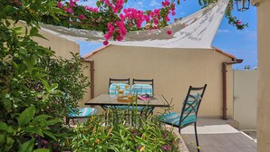 Um pátio externo com mesa e cadeiras, rodeado por plantas e flores.
