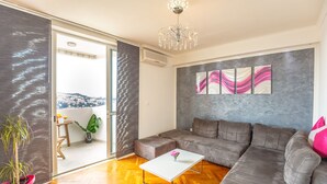 A modern living room with a grey sofa, a white coffee table, and a large window offering a view of a cityscape. - Skyscraper Apartment (Dubrovnik)