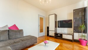 A modern living room with a grey sofa, a white coffee table, a TV, and a potted plant. - Skyscraper Apartment (Dubrovnik)