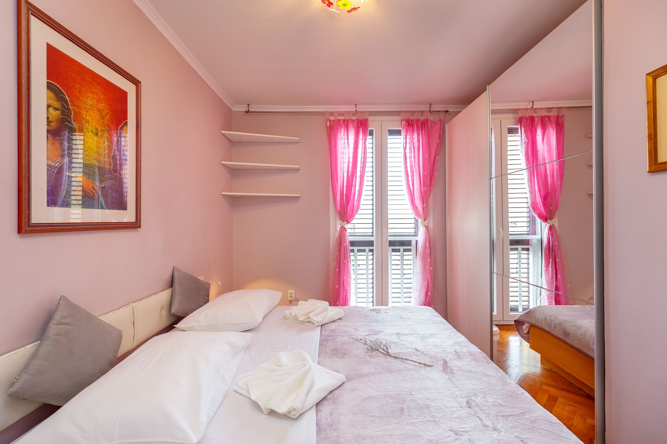 A bedroom with a bed, pillows, a painting, and pink curtains.