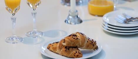 A breakfast setting with croissants on a plate, two glasses of orange juice, and a pitcher of orange juice.