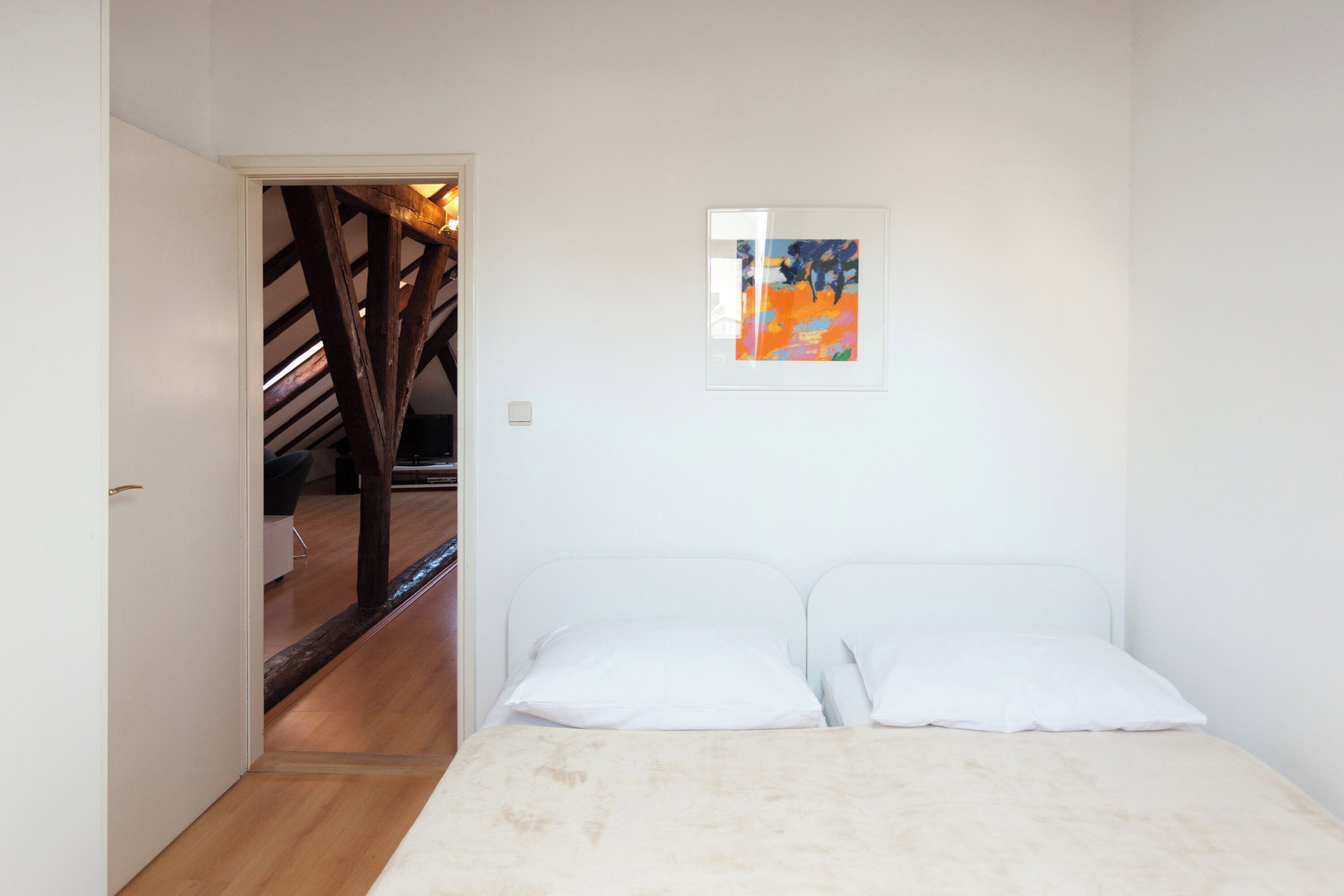 A bedroom with a bed, a door leading to a staircase, and a framed picture on the wall.
