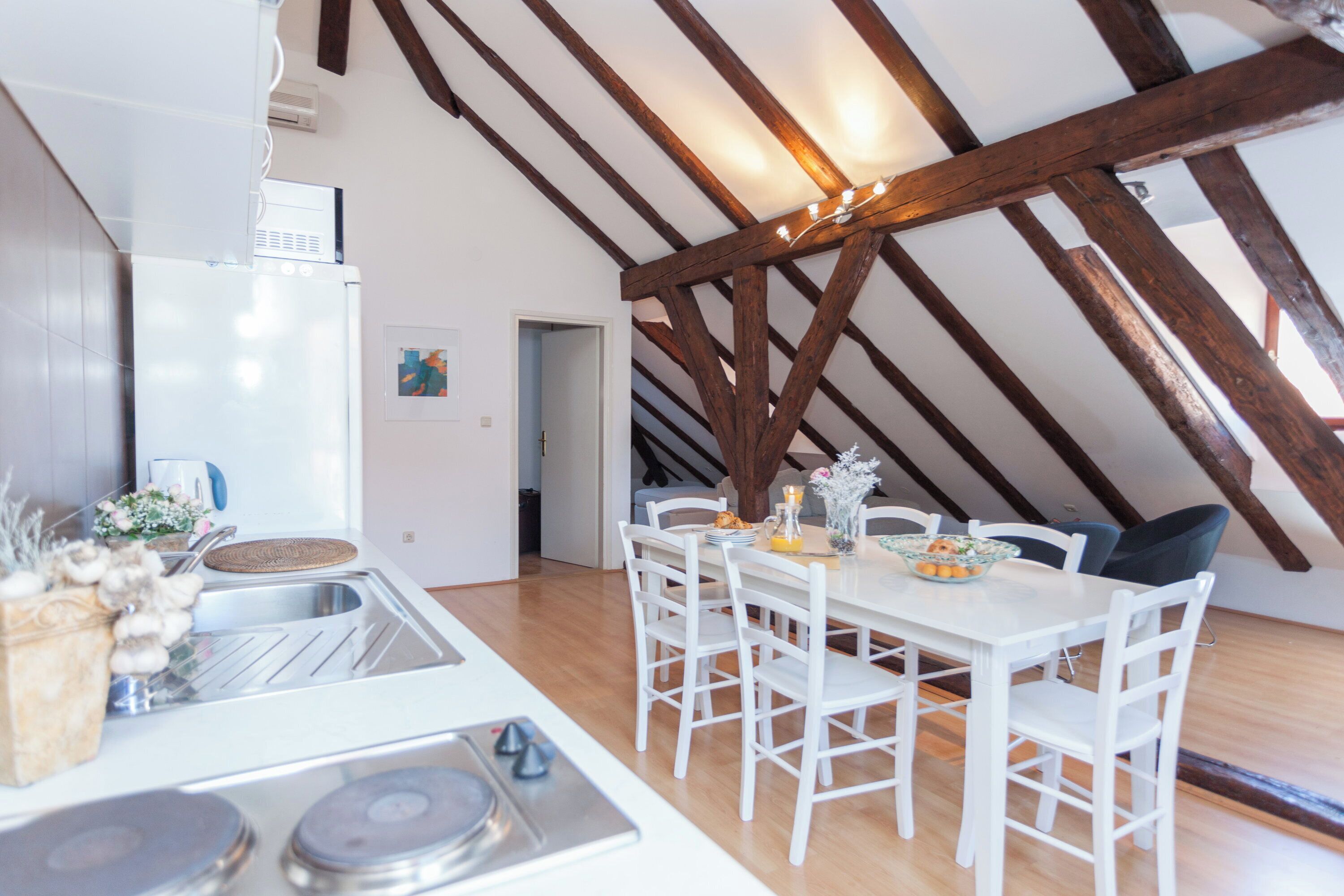 Une cuisine avec des meubles blancs, une table à manger avec des chaises et une structure de plafond en bois.