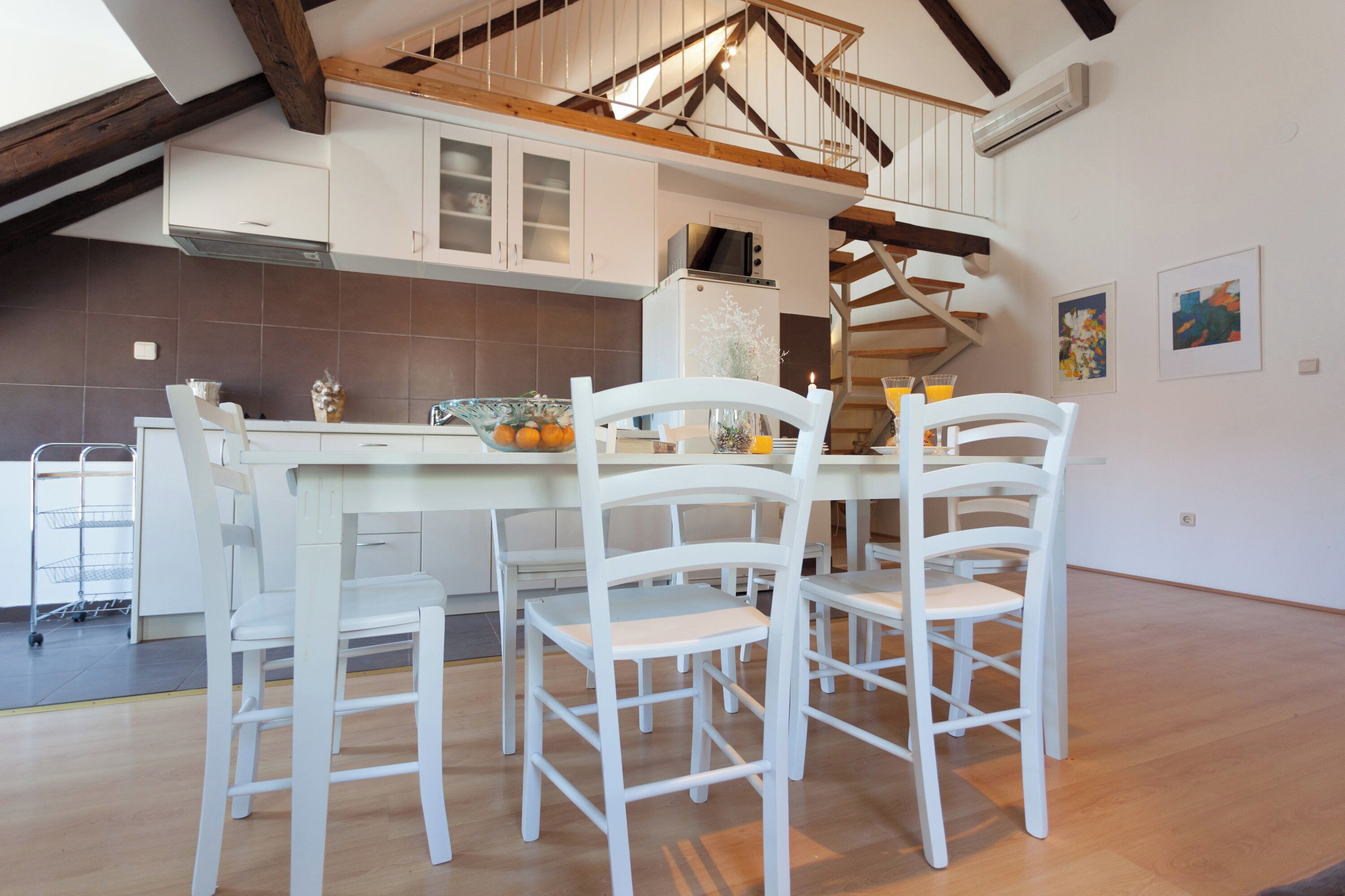 A kitchen with white cabinets, a wooden ceiling, and a dining area with white chairs.