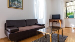 A modern living room with a dark brown sofa, a glass coffee table, a flat-screen TV on a wooden stand, and a painting on the wall. - Hedera Estate, Hedera A27 (Dubrovnik)