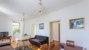 A modern living room with a sofa, a glass coffee table, a dining table with chairs, a TV on a stand, and framed pictures on the walls. - Hedera Estate, Hedera A27 (Dubrovnik)